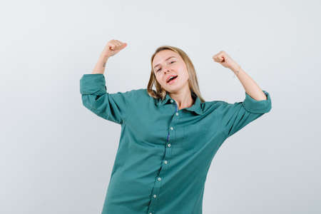 blonde woman in green shirt showing winner gesture and looking blissful , front view.の写真素材