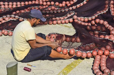 Kavala, Greece - September 23rd 2012: unidentified fisherman at work in the harbour, repair the net for next rideのeditorial素材