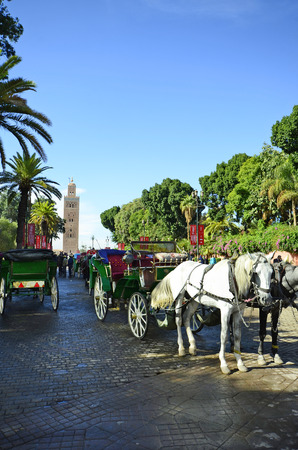Marrakesh, Morocco - November 23nd 2014: Unidentified people and horse drawn coaches between Koutoubia mosque and Djemaa el-Fna squareのeditorial素材