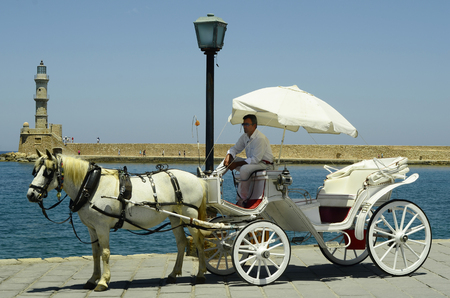 Chania, Greece - May 27th 2014: Unidentified people and horse drawn coach in front of  Venetian lighthouse in the harbor of the medieval village in Creteのeditorial素材