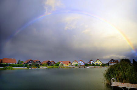 Austria, rainbow and thunder clouds over settlement with lakeの写真素材
