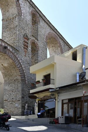 Kavala, Greece - June 13, 2019: Unidentified man and tiny cafe beside the medieval aqueduct Kamaresのeditorial素材