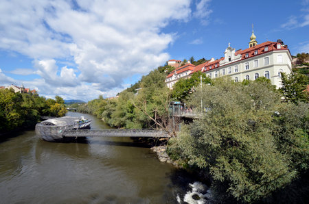 Graz, Austria - September 22, 2022: The so-called Murinsel was built on the occasion of the appointment as the cultural capital in 2003 and is located in the Mur river and a landmark as Uhrturm - Clock Tower on Schlossberg Hill.のeditorial素材