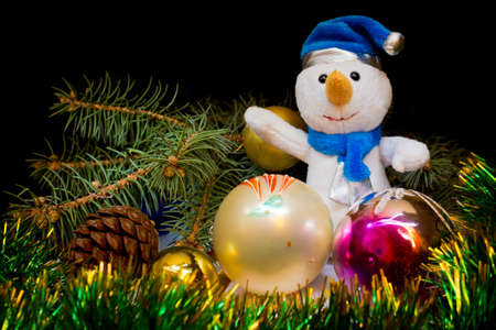 Dressed in a blue hat and scarf snowman surrounded by Christmas toys, shiny green tinsel and Christmas trees on a black backgroundの写真素材