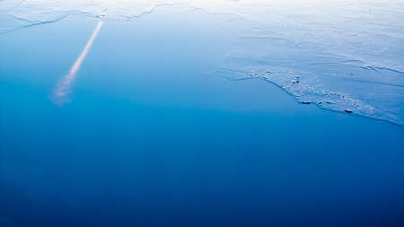 Thin ice in the water reflecting the clear blue sky の写真素材
