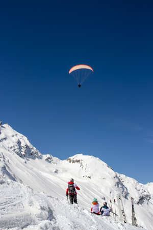 Group of skiers watch paraglider flying high in the mountains on a sunny day in winter.の写真素材
