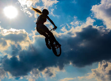 Silhouette woman cyclist flying in the sun and cloudy skyの写真素材