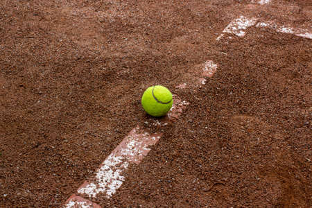 Yellow ball and Old tennis court surface is red and ruined the line markingの写真素材