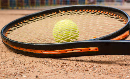 Detail of a Tennis racket and yellow ball on a red court