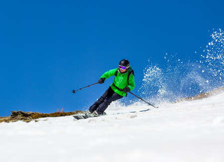 Woman skier at high speed in deep snow in a turn raises the snow dustの写真素材