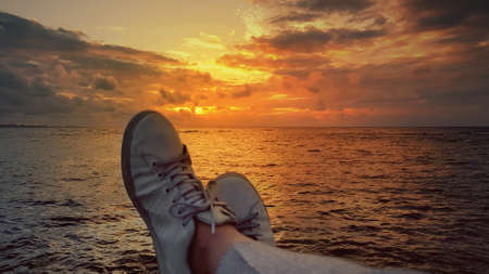 White sneakers of a man who admires the sea and the sky with a reddish glow in the island of...
