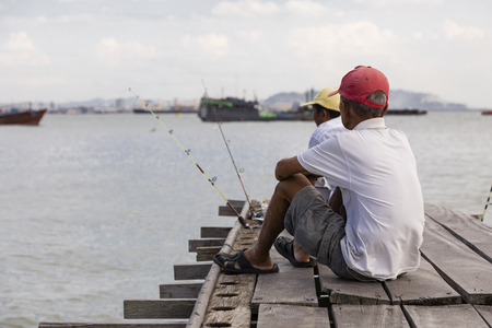 Penang, Malaysia, December 19 2017: Two Fishermen waiting for the catch of day on the wooden jetty in Georgetownのeditorial素材