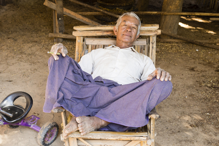 Bagan, Myanmar, December 27, 2017:  Senior man recovers in an armchair and smokes a cigaretteのeditorial素材