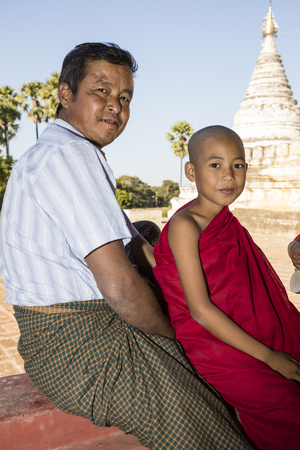 Bagan, Myanmar, December 29, 2017:  Father and son as a Buddhist novice are sitting smiling in front of a pagoda in Bagan, Myanmarのeditorial素材