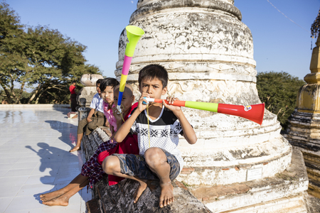 Bagan, Myanmar, December 29, 2017:  Group of children are sitting in front of a stupa and making noise with vuvuzelas in Bagan, Myanmarのeditorial素材