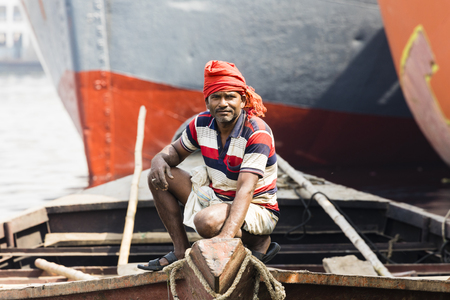 Dhaka, Bangladesh, February 24 2017: Portrait of a rower waiting for passengers in his wooden boat in Dhaka, Bangladesh. In the background you can see the bow of shipsのeditorial素材