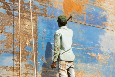 Dhaka, Bangladesh, February 24 2017: A worker at a shipyard in Dhaka Bangladesh beats the rust from the hull with a hammerのeditorial素材