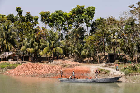 Morrelganj, Bangladesh, February 27 2017: At the riverside in Bangladesh, bricks are being unloaded from an old wooden boatのeditorial素材