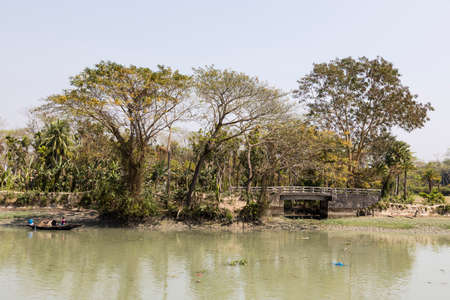 Morrelganj, Bangladesh, February 27 2017: Tropical river landscape with a small wooden boat in Bangladeshのeditorial素材