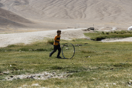 Bulunkul, Tajikistan, August 23 2018: A child in the village of Bulunkul in the Pamir mountains plays with an old bicycle rimのeditorial素材