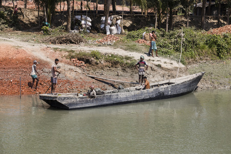 Morrelganj, Bangladesh, February 27 2017: At the riverside in Bangladesh, bricks are being unloaded from an old wooden boatのeditorial素材