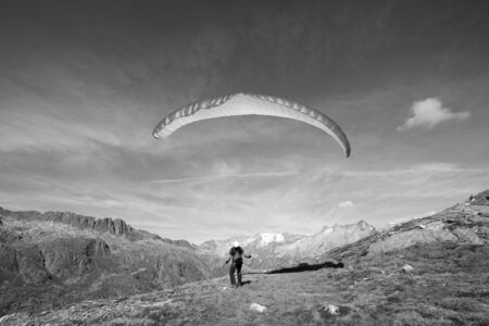 Paraglider pilot stands on a rock and balances his paraglider above his head near Grimsel in the Swiss Alpsの写真素材