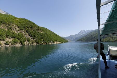 Koman, Albania, July 7 2019: A tourist sits on the railing and enjoys the scenery on the Komani lake in the dinaric alps of Albaniaのeditorial素材