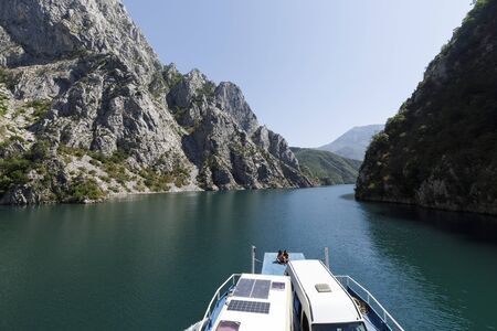 Koman, Albania, July 7 2019: A couple sitting on the boat ramp enjoying the landscape with mountains and green forests on a boat trip on the Komani lake in the dinaric alps of Albaniaのeditorial素材