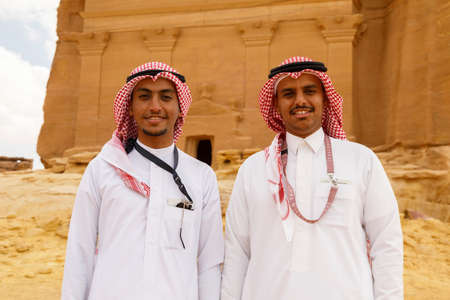 AlUla, Saudi Arabia, February 19 2020: Two young Saudi Arabian tour guides pose in front of the tomb of Lihyan son of Kuza, known as Qasr AlFarid, the most iconic tomb in AlUla in the region of Mada'in Saleh, Saudi Arabiaのeditorial素材