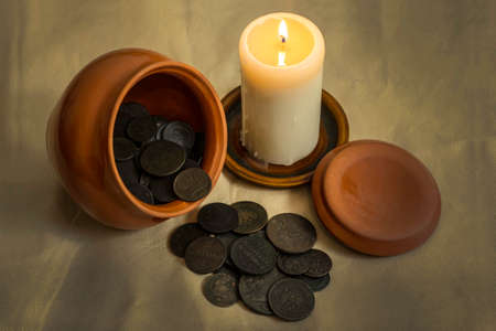 The hoard of copper coins of the Russian Empire in a clay pot. A burning candle.