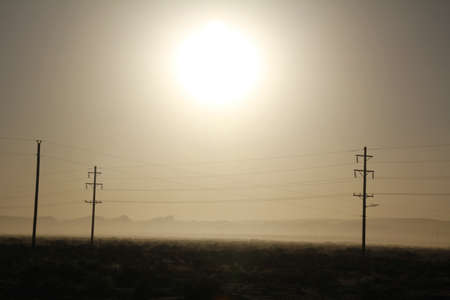 Silouette of communication and electrical towers backlit by the sun in a dry New Mexico landscapeの写真素材