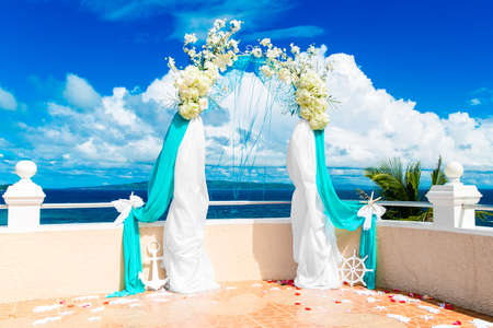 Wedding ceremony on a tropical beach in blue. Arch decorated with flowers on hotel, tropical sea in the background. Wedding and honeymoon concept.の写真素材