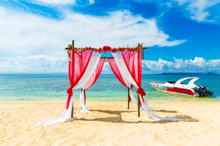 Wedding ceremony on a tropical beach in red. Arch decorated with flowers on the sandy beach. Wedding and honeymoon concept.の写真素材