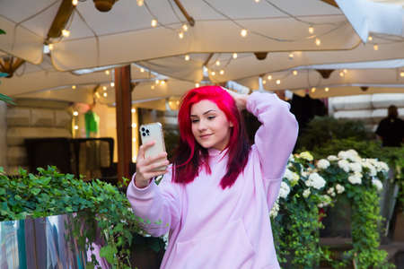 Beautiful red-haired girl takes selfie on smartphone on city street