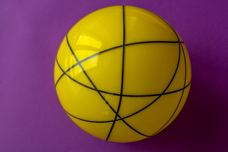 Big yellow glass ball on a violet background. Still life of striped yellow ball on bright violet table.の写真素材