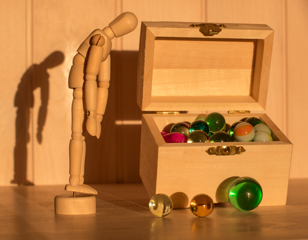 Sad wooden man in front of a chest with colored glass balls,. wooden doll and treasure chest.の写真素材
