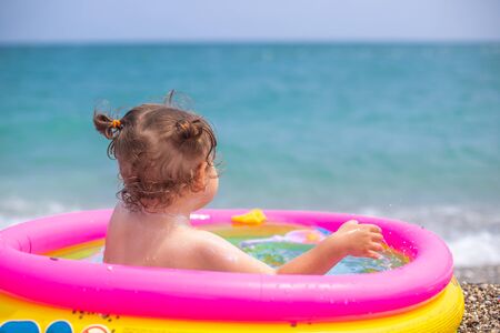 A little girl is playing an inflatable pool. Cute baby in an inflatable pool against the backdrop of the blue seaの写真素材
