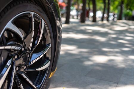 The front of the sports car. Wheel of a sports car on the background of a blurred sidewalk in a...