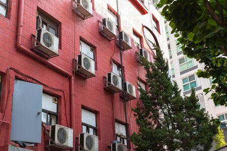 High-rise building from the yard. Facade is made of red tiles, an iron door, a pipe and wires stick out. Air conditioning on the wall.の写真素材