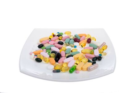 A pile of multi-colored pills on a white plate symbolizing food. Vitamins on a white isolated...
