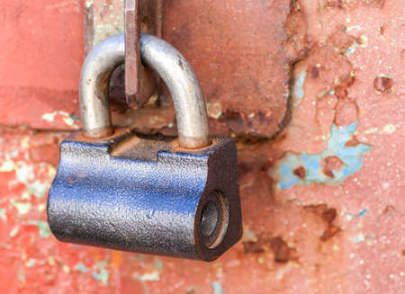Padlock on old rusty red metal door