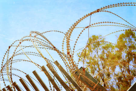 Security with a barbed wire fence with blue sky. Photo textured in old color image style.の写真素材