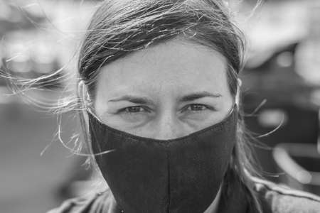 A middle-aged woman in a medical mask looks into the camera. Monochrome photography with a small...