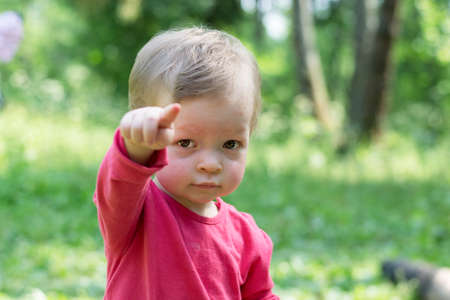 Child in a red shirt looks sternly at the camera and points an imperious finger.の写真素材