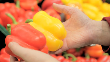 Women hands with red and yellow paprika in their hands. A woman in the store chooses vegetables. The concept of vegetarianism and healthy eatingの写真素材