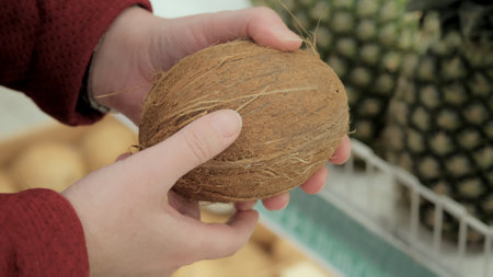 Woman in the store chooses a coconut. Shelves of pineapples can be seen in the background. Closeup shotの写真素材