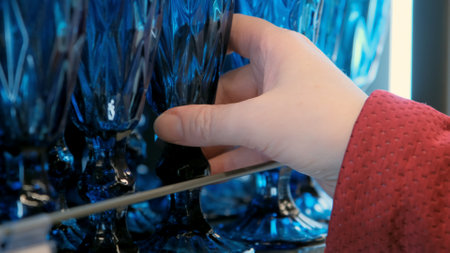 Buying dishes in store. Hand girl takes a blue wine glass from the supermarket shelf. Camera shoots...