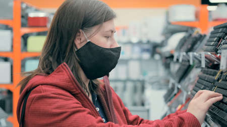 Caucasian a woman in mask against virus chooses computer keyboard in store. Concept of shopping and...