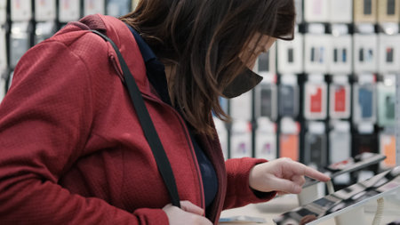 Girl in the mask against the virus chooses a tablet in the store of electronic gadgets and devices. Screen from video footageの写真素材