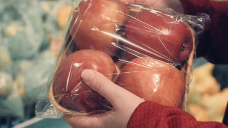 Women hands in the store choose a package with red apples. Close up shot. The concept of shopping, vegetarianism, consumption of fruits and vitaminsの写真素材